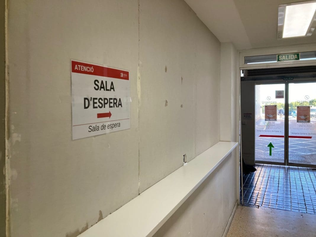 Cartel de Sala de Espera con distintivos de la Generalitat Valenciana sobre la pared de un pasillo. Al fondo se ve la puerta