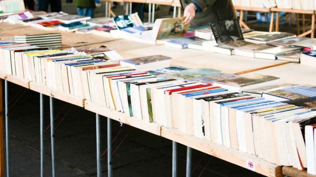 imagen de lomos de libros sobre una mesa de patas metálicas y al fondo unas manos abriendo uno de los libros