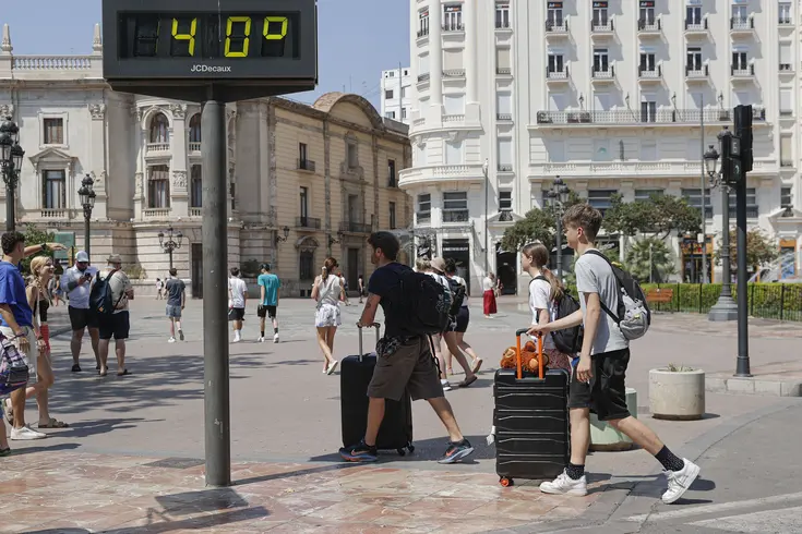 Turistas con maletas junto a un termómetro urbano que marca 40 grados en València